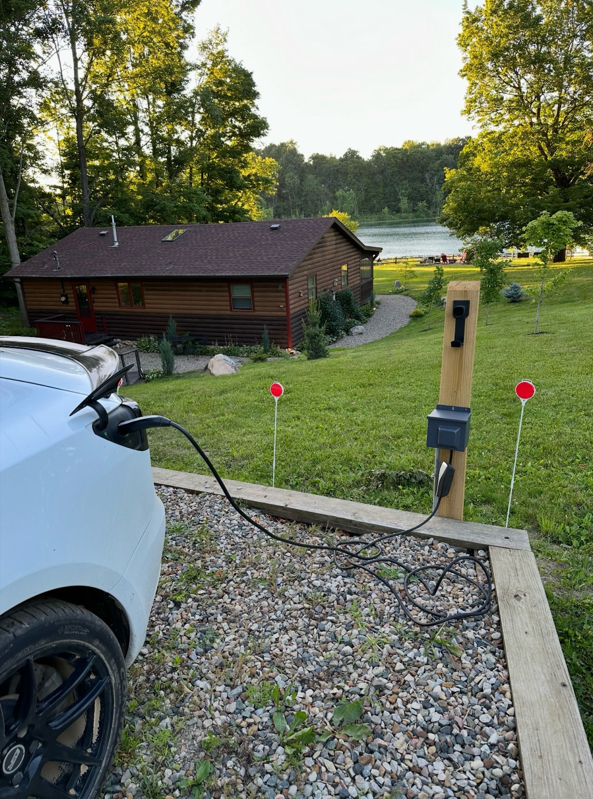 An electric car charging at the on-site station with the cabin and lake beyond