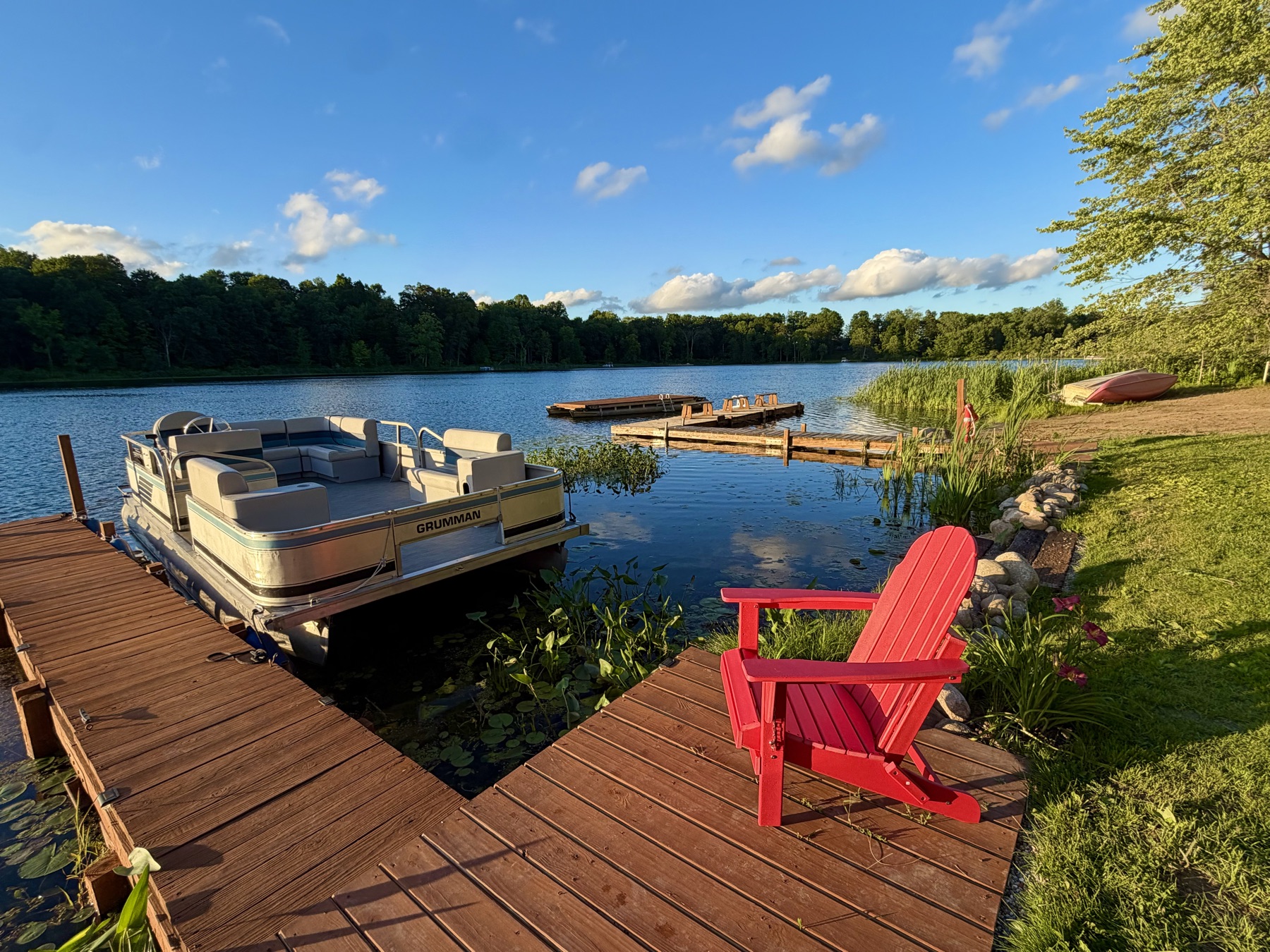 The pontoon moored at the dock with a red Adirondack chair in evening light